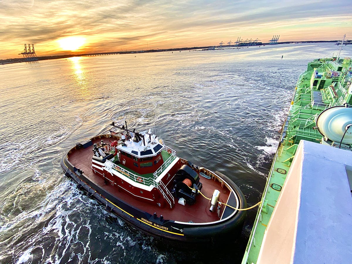The tug Rosemary McAllister pushes along the side of a ship with a glorious sunset in the Port of Virginia.