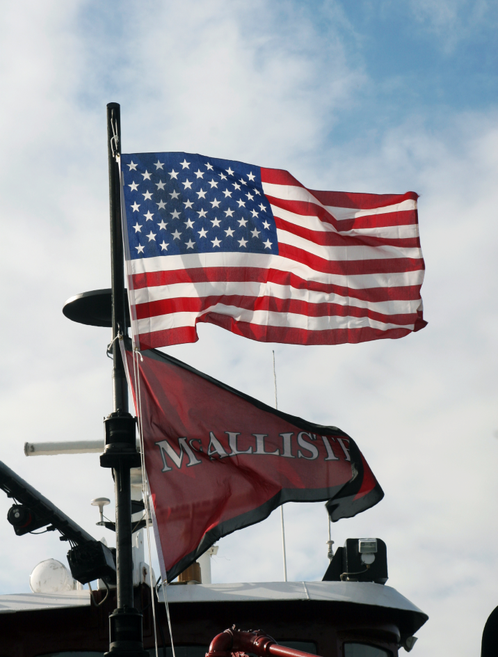 The American flag and McAllister flag fly from the mast of a tugboat